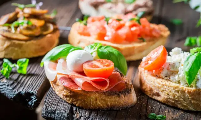 Verschiedene herzhafte Snacks auf geröstetem Brot: Bruschetta mit Tomaten, Pilzen, Schinken und Mozzarella.