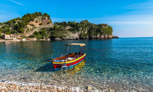 Barca colorata in un mare cristallino, ideale per scoprire cosa fare a Ferragosto in Sicilia, tra scogliere verdi e borghi pittoreschi.