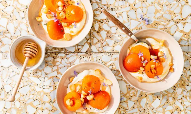 Trois bols de compote abricot onctueuse, garnie d'amandes et de fleurs violettes. Un pot de miel avec sa cuillère est à côté.