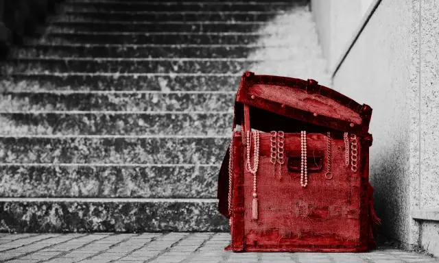 Czerwona skrzynia z biżuterią, stojąca na schodach. To pamiątka, spadek po rodzicach, pełen wspomnień.