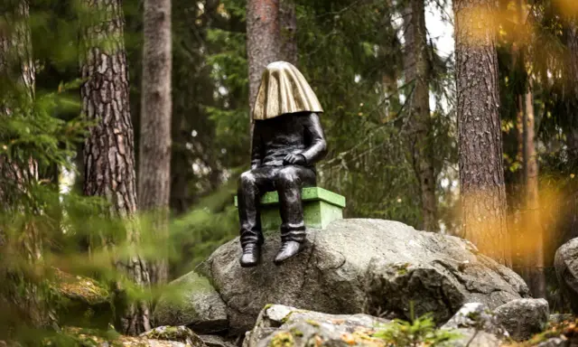 En mystisk staty med gyllene tyg över huvudet sitter på en sten i **stadsparken Falun**.