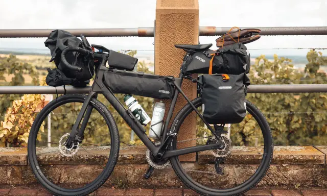 Bereit für die nächste gravel tour: Ein voll beladenes Gravelbike mit Ortlieb-Taschen, Trinkflaschen und sogar Schuhen auf dem Gepäckträger.