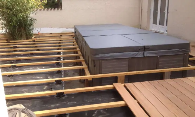 Construction d'une terrasse en bois autour d'un spa. L'espacement des plots sur le plot béton est visible, prêt pour les lames de bois.