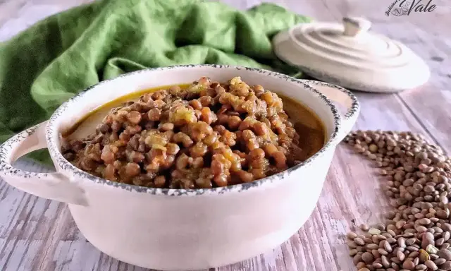 Un invitante piatto di lenticchie in umido, servito in una ciotola rustica, con un panno verde sullo sfondo.