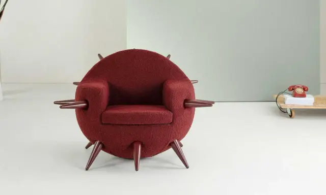 A round, burgundy armchair with pointed legs and armrests, in a minimalist room.