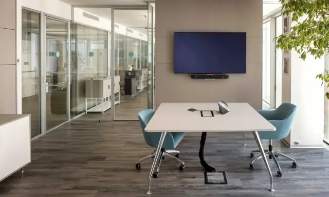 Un bureau futuriste avec une table de réunion, des chaises bleues, un écran mural et des cloisons vitrées.