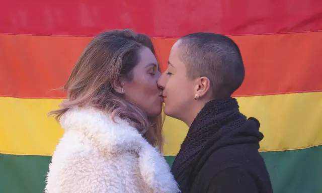 Deux femmes s'embrassent tendrement devant un drapeau arc-en-ciel, une belle représentation de l'amour saphique.
