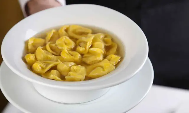 Un piatto fumante di tortellini in brodo, un classico comfort food italiano, servito in una ciotola bianca.
