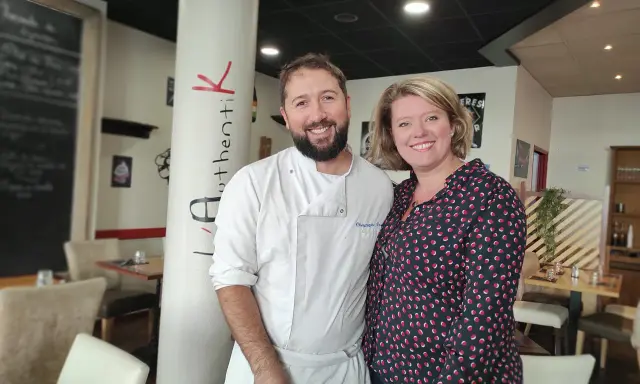 Le chef et sa collègue sourient devant la colonne "Authentik St Grégoire". L'ambiance chaleureuse du restaurant est palpable.