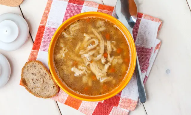Aromaticzne flaki po zamojsku w pomarańczowej misce, obok kromka chleba i łyżka. Pyszne danie gotowe do spożycia.