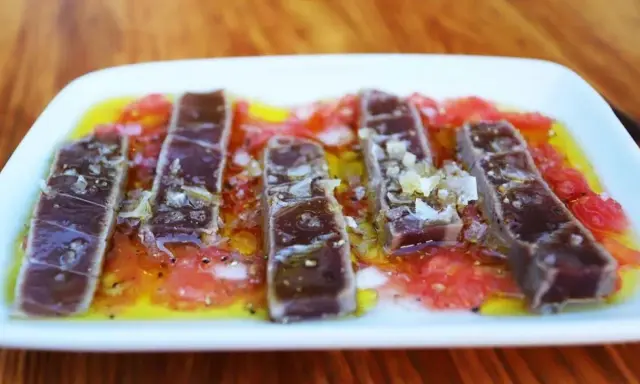 Tiras de atún marinado sobre rodajas de tomate y cítricos, un delicioso plato de comida típica de Huelva.