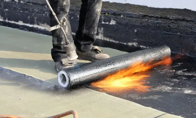 Un couvreur utilise un chalumeau pour souder un rouleau de membrane bitumineuse, créant ainsi une toiture chaude et étanche.