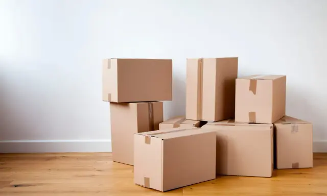 Stapel von braunen Kartons auf einem Holzboden, bereit für den Umzug oder zur Aufbewahrung.