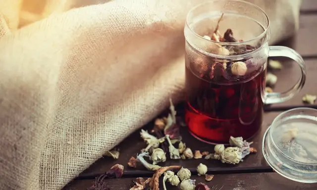 Infusion rouge dans une tasse en verre, entourée d'herbes séchées. Un remède naturel diurétique à portée de main.