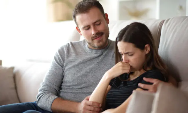 Un homme réconforte une femme en pleurs, son regard suggère une manipulation subtile, un exemple de pervers narcissique.