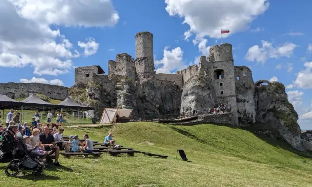 Ruiny zamku na skale, część wyżyny krakowsko-częstochowskiej, z widownią siedzącą na trawie.