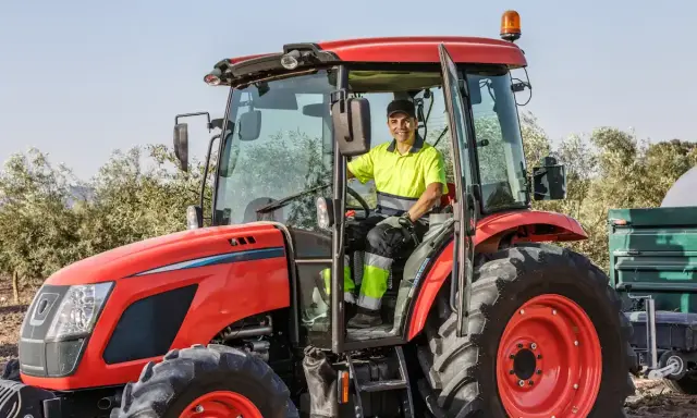 Un homme souriant conduit un tracteur rouge, une machine pour arracher des bambous, prêt à travailler dans un champ.