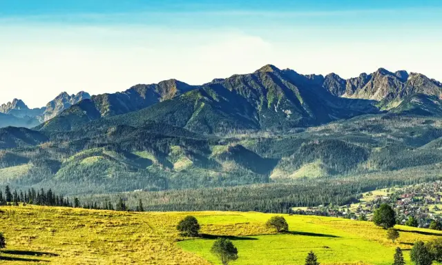 Widok na Tatry po angielsku: zielone wzgórza, lasy i skaliste szczyty. W oddali widać małą wioskę.