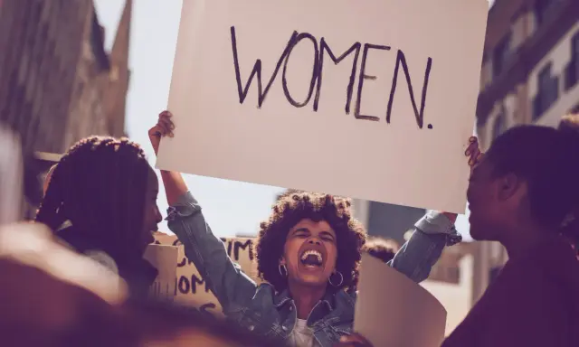 Frauen demonstrieren für Gleichberechtigung. Eine Frau hält ein Schild mit der Aufschrift "WOMEN". Das zeigt, was feminist ist: eine Stimme für Frauen.
