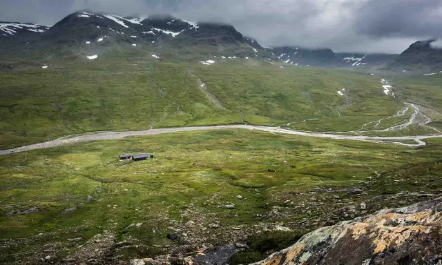 Vacker vy över fjällandskap med snöklädda toppar, en slingrande älv och stugor vid Kungsleden nära Hemavan.
