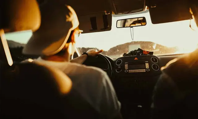 Hombre con gorra al volante, listo para planificar viaje en coche. El sol ilumina el interior del vehículo.