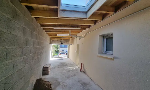 Vue d'une extension en cours de construction avec reprise de toiture, poutres apparentes et un puits de lumière.