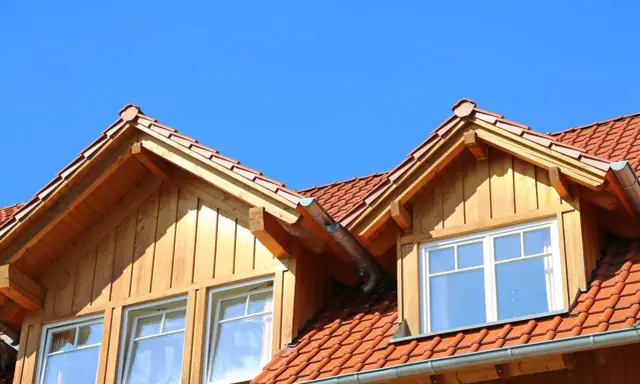 Holzverkleideter Dachausbau mit Gaube und roten Ziegeln unter blauem Himmel.
