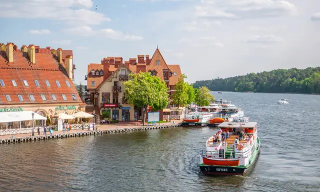 Port w Mikołajkach z zacumowanymi statkami i kamieniczkami. Wspaniałe mikołajki atrakcje dla turystów.
