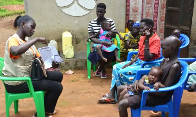 Kvinnor och barn samlas för vaccination i Uganda. En kvinna i väst visar upp papper.
