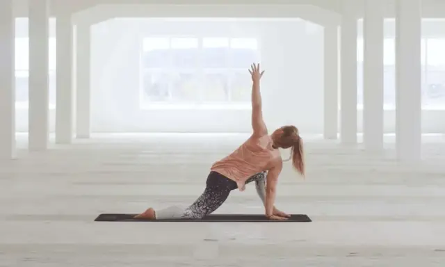 Kvinna utför en vriden yogaställning i ett ljust, öppet rum. Hon fokuserar på sin power yoga-träning.