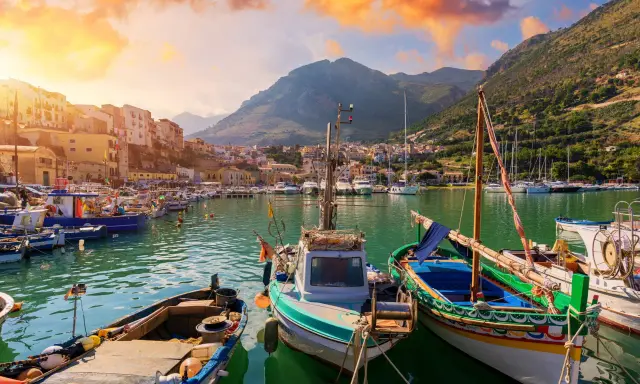 Malowniczy port w Trapani, idealne miejsce na zwiedzanie. Łodzie kołyszą się na wodzie, a w tle widać góry i kolorowe budynki.