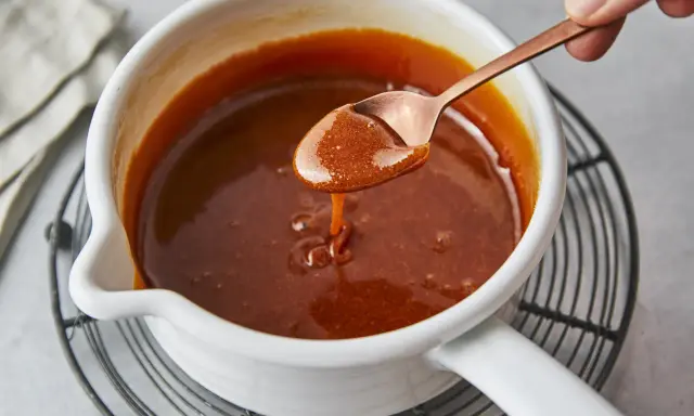 Flüssiges Karamell tropft von einem Löffel in einen Topf. Das Zucker karamellisieren ist fast perfekt.