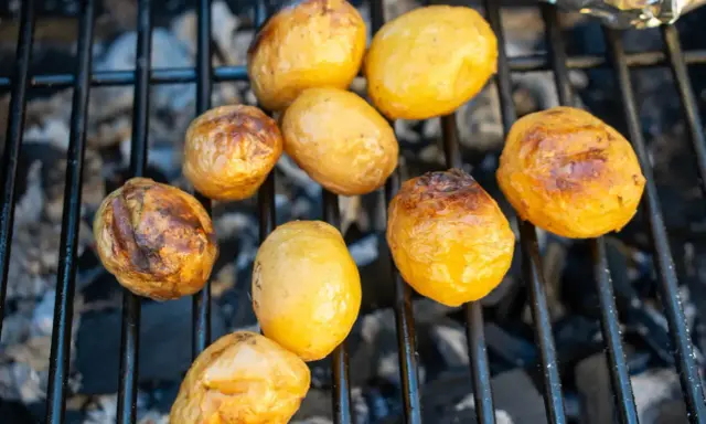 Kleine, goldbraune Kartoffeln garen auf dem Grillrost über glühender Kohle. Sie sind bereit für ein leckeres Abendessen.