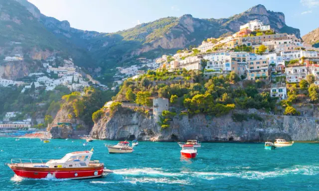 Barche a vela navigano nelle acque turchesi davanti alle case colorate aggrappate alle scogliere delle isole costiera amalfitana.