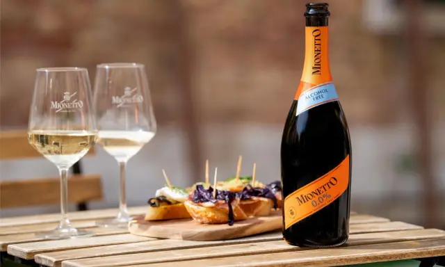 Mionetto alkoholfreier Aperol 0.0% mit zwei Gläsern und leckeren Bruschettas auf einem Holztisch.
