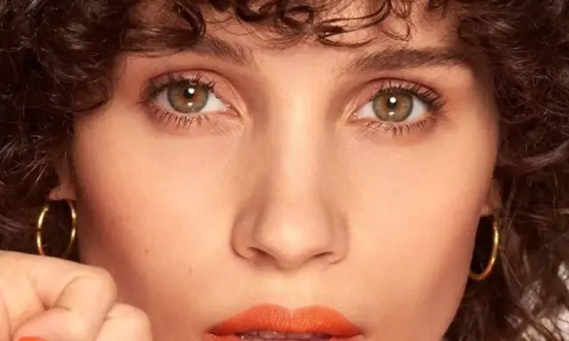 Primer plano de una mujer con rizos oscuros y maquillaje color coral vibrante en los labios.