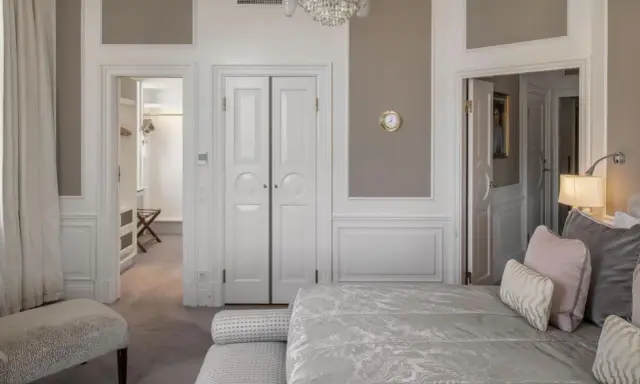 Ett elegant sovrum med en lyxig säng, en öppen garderob och en kristallkrona. Wilhelmina Skogh skulle trivas här.