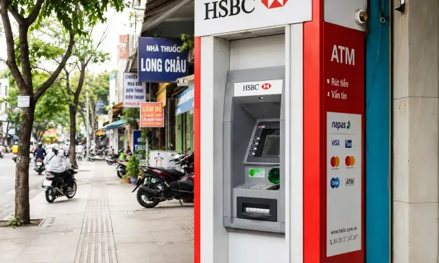Bankomat HSBC w Hanoi, gotowy do wypłaty waluty. W tle widać ruchliwą ulicę z motocyklami i sklepami.