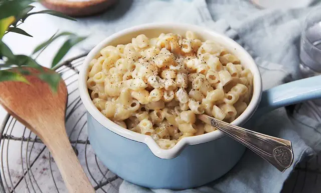 En skål med krämiga stuvade makaroner, toppad med svartpeppar. En träsked ligger bredvid.
