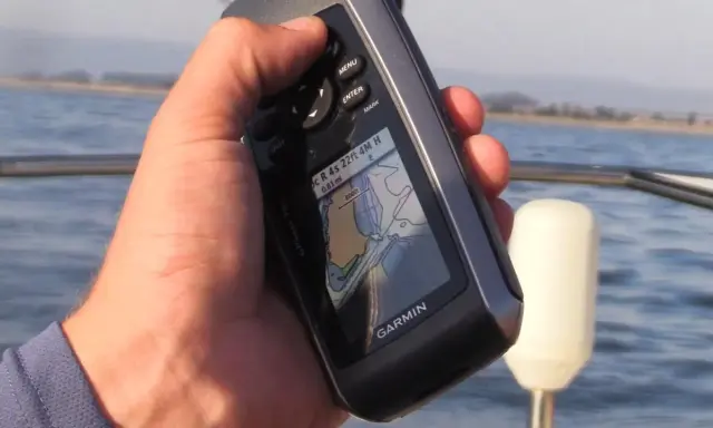 Main tenant une carte GPS Garmin sur un bateau, naviguant sur l'eau.