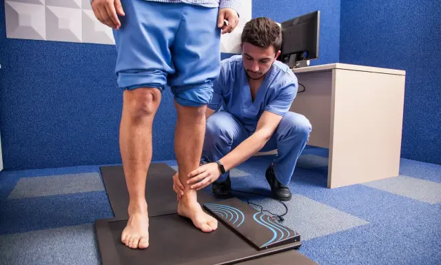 Un podologue examine le pied d'un patient sur un tapis de mesure, dans le cadre d'une consultation de pédicurie.