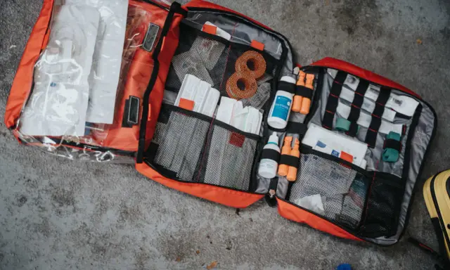 Rozłożona apteczka turystyczna wyposażenie: plastry, bandaże, płyn dezynfekujący, igły, strzykawki i inne akcesoria medyczne.