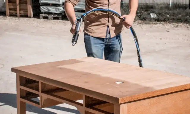 Un homme utilise un appareil pour le décapage bois sur un bureau. La surface est partiellement nettoyée, révélant le bois brut.