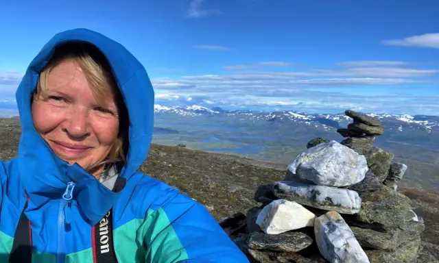 Kvinna på berg i Sverige med en stenröse i förgrunden och snöklädda berg i bakgrunden.