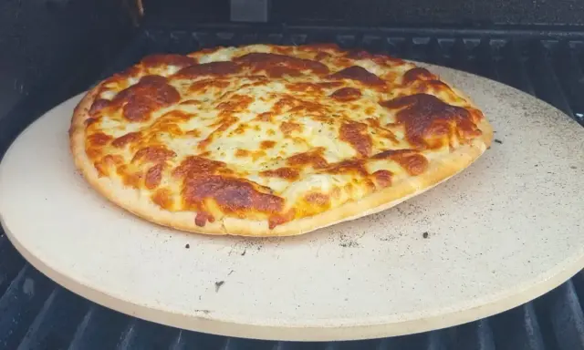 Upieczona pizza z roztopionym serem na kamieniu do pizzy na grillu.