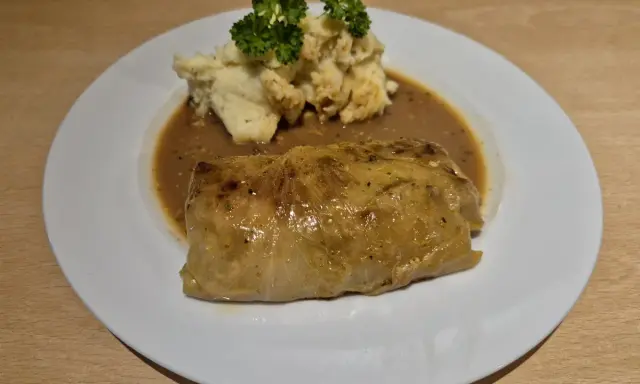 Ein herzhaftes Krautwickel Rezept auf einem Teller mit Kartoffelbrei und Sauce, garniert mit Petersilie.