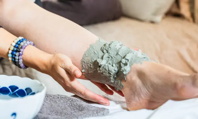 Application d'un cataplasme d'argile verte sur une jambe, pour un soin détoxifiant et apaisant.