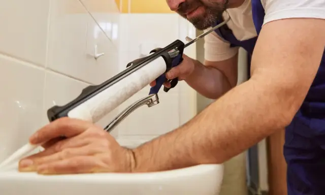 Un homme applique une bonde silicone autour d'un lavabo avec un pistolet.