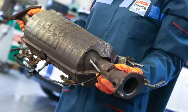 Mechanik w rękawiczkach trzyma zużyty katalizator, prawdopodobnie z Peugeota p2448.