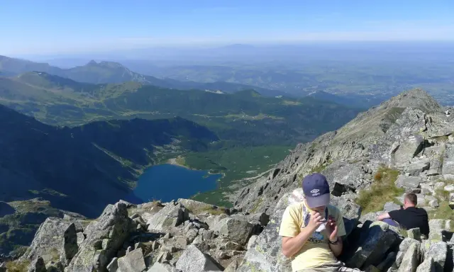 Widok na Tatry z żlebu Kulczyńskiego. W dole jezioro, na pierwszym planie odpoczywający turyści.